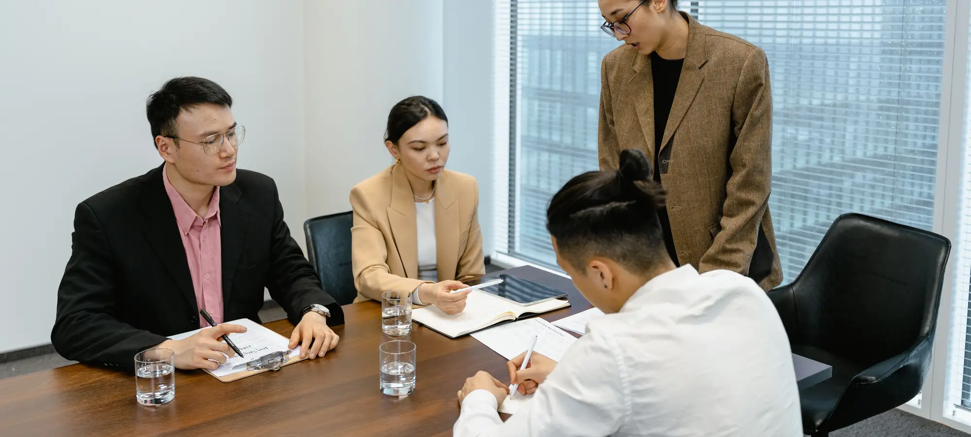 A team seated around a meeting-room table taking notes beside a bright office window