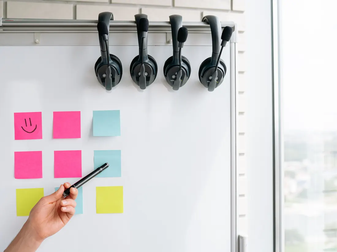 A hand pointing a marker at a grid of pink, blue and yellow sticky notes on a whiteboard