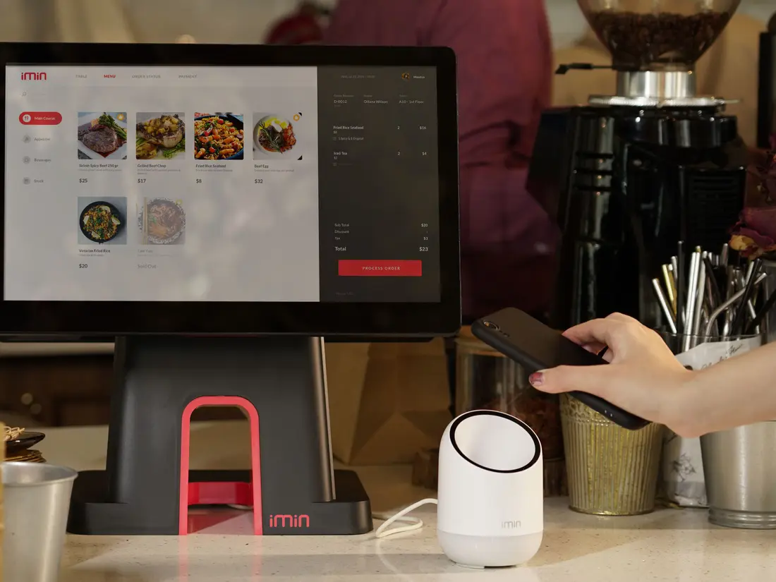 A point-of-sale terminal on a café counter beside a customer paying